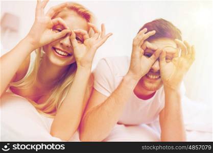 people, rest, love, relationships and fun concept - happy couple lying in bed at home and making finger glasses
