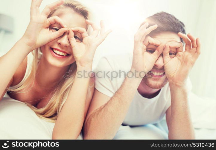 people, rest, love, relationships and fun concept - happy couple lying in bed at home and making finger glasses. happy couple lying in bed at home