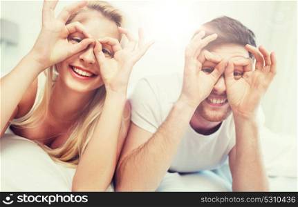 people, rest, love, relationships and fun concept - happy couple lying in bed at home and making finger glasses. happy couple lying in bed at home