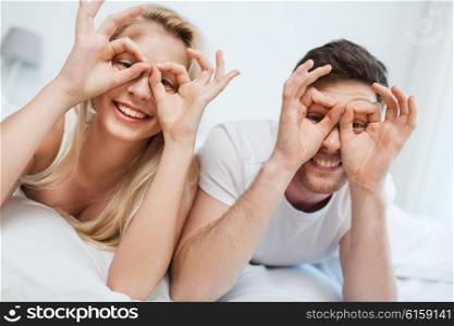 people, rest, love, relationships and fun concept - happy couple lying in bed at home and making finger glasses