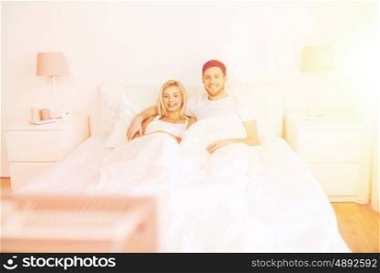 people, rest, love, relationships and happiness concept - happy couple lying in bed at home and watching tv
