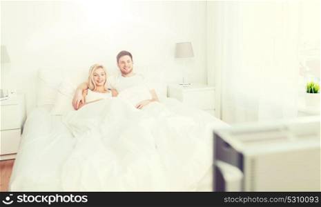 people, rest, love, relationships and happiness concept - happy couple lying in bed at home and watching tv. happy couple lying in bed at home and watching tv