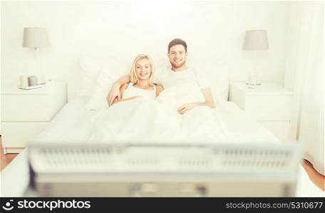 people, rest, love, relationships and happiness concept - happy couple lying in bed at home and watching tv. happy couple lying in bed at home and watching tv