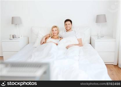 people, rest, love, relationships and happiness concept - happy couple lying in bed at home and watching tv
