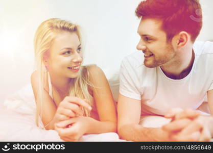 people, rest, love, relationships and happiness concept - happy couple lying in bed at home