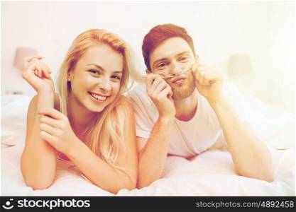 people, rest, love, relationships and happiness concept - happy couple lying in bed at home