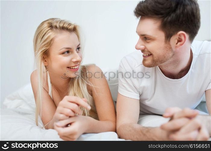 people, rest, love, relationships and happiness concept - happy couple lying in bed at home