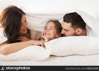 people, rest, love, relationships and happiness concept - happy family lying in bed under blanket at home