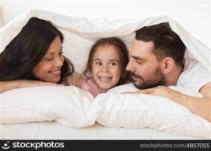 people, rest, love, relationships and happiness concept - happy family lying in bed under blanket at home