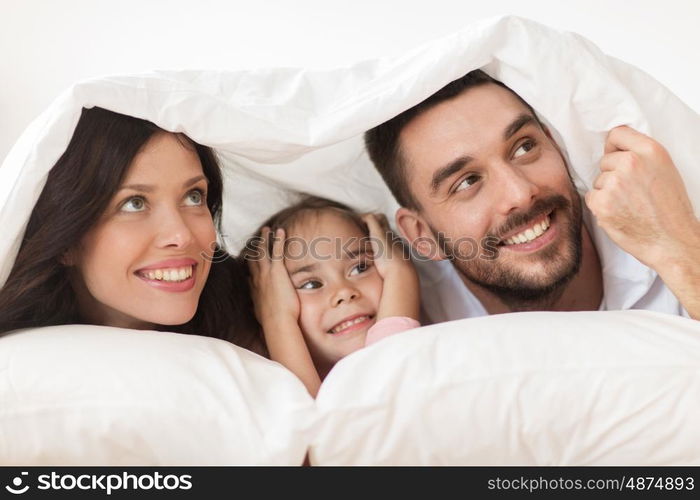 people, rest, love, relationships and happiness concept - happy family lying in bed under blanket at home