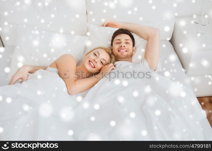 people, rest, love, relationships and happiness concept - happy smiling couple lying in bed at home over snow