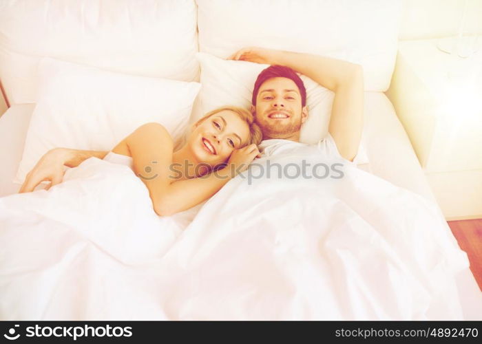 people, rest, love, relationships and happiness concept - happy smiling couple lying in bed at home