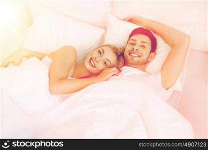 people, rest, love, relationships and happiness concept - happy smiling couple lying in bed at home. happy couple lying in bed at home