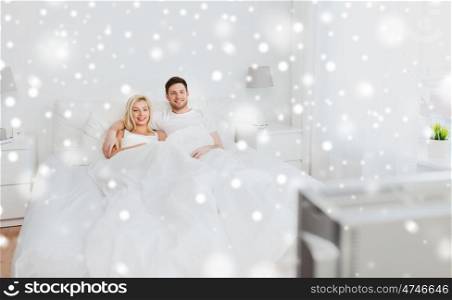 people, rest, love, television and entertainment concept - happy smiling couple lying in bed and watching tv at home over snow