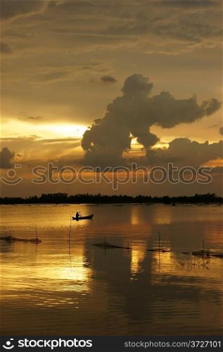 People rowing the row boat on river at sunrise, cloudscape with clouds as gorilla shape on the yellow sky