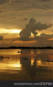 People rowing the row boat on river at sunrise, cloudscape with clouds as gorilla shape on the yellow sky