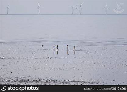 People running on beach, wind farm in distance