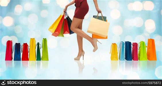 people, sale and consumerism concept - close up of woman in red short skirt and high heeled shoes with shopping bags over blue holidays lights background