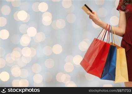 people, sale and consumerism concept - close up of woman with shopping bags and bank or credit card over holidays lights background