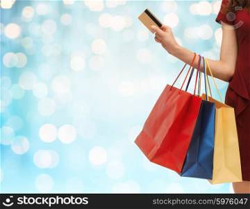 people, sale and consumerism concept - close up of woman with shopping bags and bank or credit card over blue holidays lights background