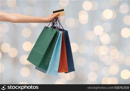 people, sale and consumerism concept - close up of woman with shopping bags and bank or credit card over holidays lights background