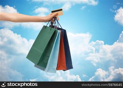 people, sale and consumerism concept - close up of woman with shopping bags and bank or credit card over blue sky and clouds background