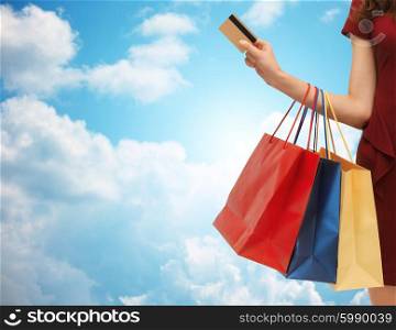 people, sale and consumerism concept - close up of woman with shopping bags and bank or credit card over blue sky and clouds background