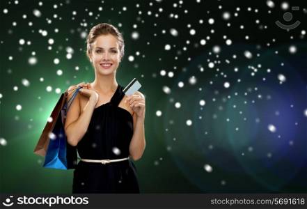 people, sale, banking, money and holidays concept - smiling woman in dress with shopping bags and credit card over snow and night lights background
