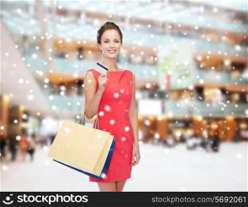 people, sale, christmas and holidays concept - smiling elegant woman in red dress with bags and plastic card over shopping center background