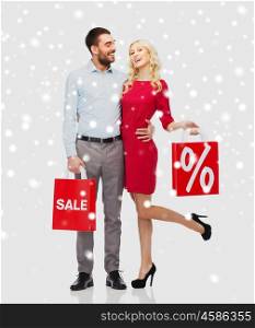 people, sale, christmas, winter and holidays concept - happy couple with red shopping bags hugging over snow background