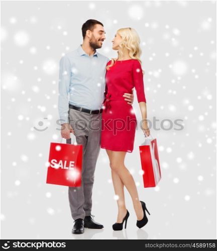 people, sale, christmas, winter and holidays concept - happy couple with red shopping bags hugging and talking over snow background
