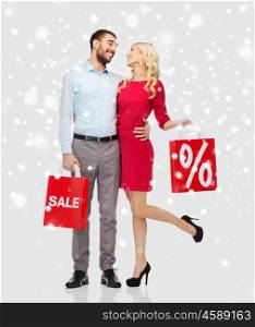 people, sale, christmas, winter and holidays concept - happy couple with red shopping bags hugging and talking over snow background