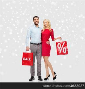 people, sale, christmas, winter and holidays concept - happy couple with red shopping bags hugging over snow background