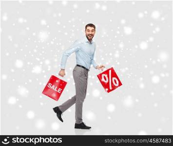 people, sale, christmas, winter and holidays concept - smiling man holding red shopping bags with percentage sign over snow background