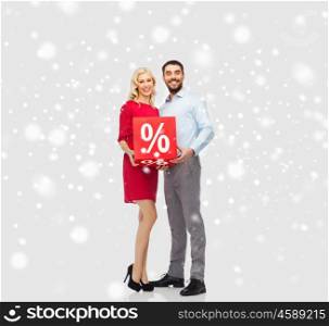 people, sale, christmas, winter shopping and holidays concept - happy couple with red percentage sign over snow background