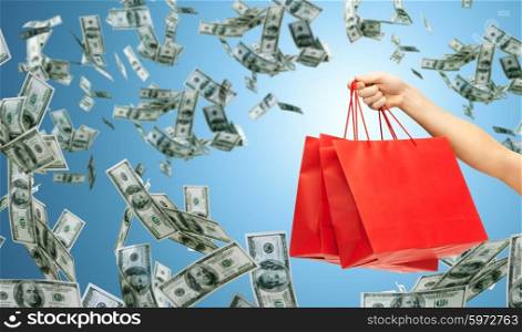 people, sale, consumerism, advertisement and finance concept - close up of hand holding red blank shopping bags over blue background and money rain