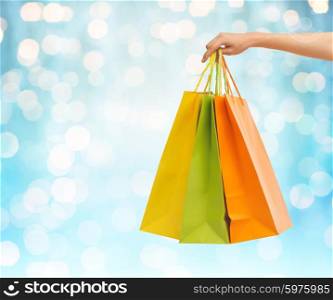 people, sale, consumerism and advertisement concept - close up of hand holding shopping bags over blue holidays lights background