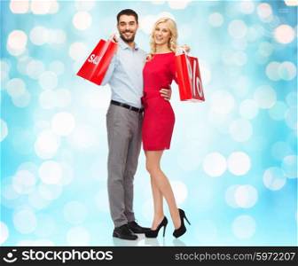 people, sale, discount and holidays concept - happy couple hugging with red shopping bags over blue holidays lights background