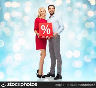 people, sale, discount and holidays concept - happy couple with red sale sign over blue lights background