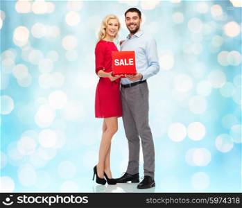 people, sale, discount and holidays concept - happy couple with red sale sign over blue holidays lights background