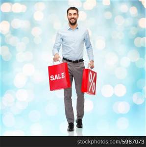 people, sale, discount and holidays concept - smiling man holding red shopping bags with percentage sign over blue lights background