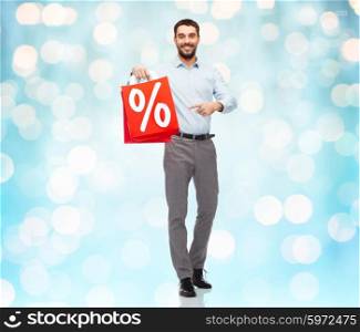 people, sale, discount and holidays concept - smiling man holding red shopping bags with percentage sign over blue holidays lights background