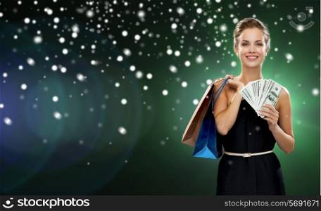 people, sale, gifts, money and holidays concept - smiling woman in dress with shopping bags and money over snow and night lights background