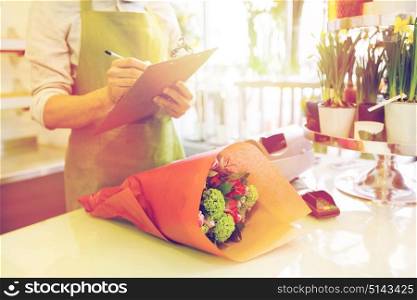 people, sale, retail, business and floristry concept - close up of florist man with clipboard and bunch writing and making notes at flower shop counter. close up of man with clipboard at flower shop