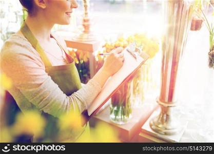 people, sale, retail, business and floristry concept - close up of happy smiling florist woman with clipboard writing and making notes order at flower shop. close up of woman with clipboard at flower shop