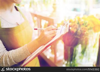 people, sale, retail, business and floristry concept - close up of happy smiling florist woman with clipboard writing and making notes order at flower shop. close up of woman with clipboard at flower shop