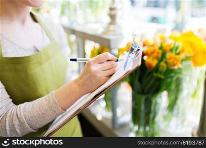 people, sale, retail, business and floristry concept - close up of happy smiling florist woman with clipboard writing and making notes order at flower shop