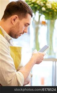 people, sale, retail, business and floristry concept - florist man texting on smartphone at flower shop