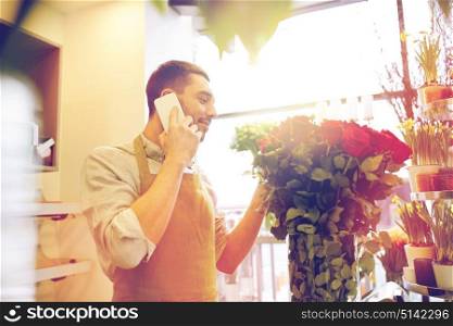 people, sale, retail, business and floristry concept - florist man with red roses calling on smartphone at flower shop counter. man with smartphone and red roses at flower shop