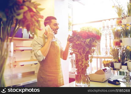 people, sale, retail, business and floristry concept - florist man with red roses calling on smartphone at flower shop counter. man with smartphone and red roses at flower shop